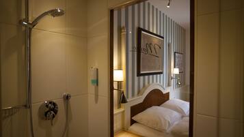Una habitación de hotel con ducha, cama, mesita de noche y pared decorada con papel tapiz a rayas y cuadros enmarcados.
