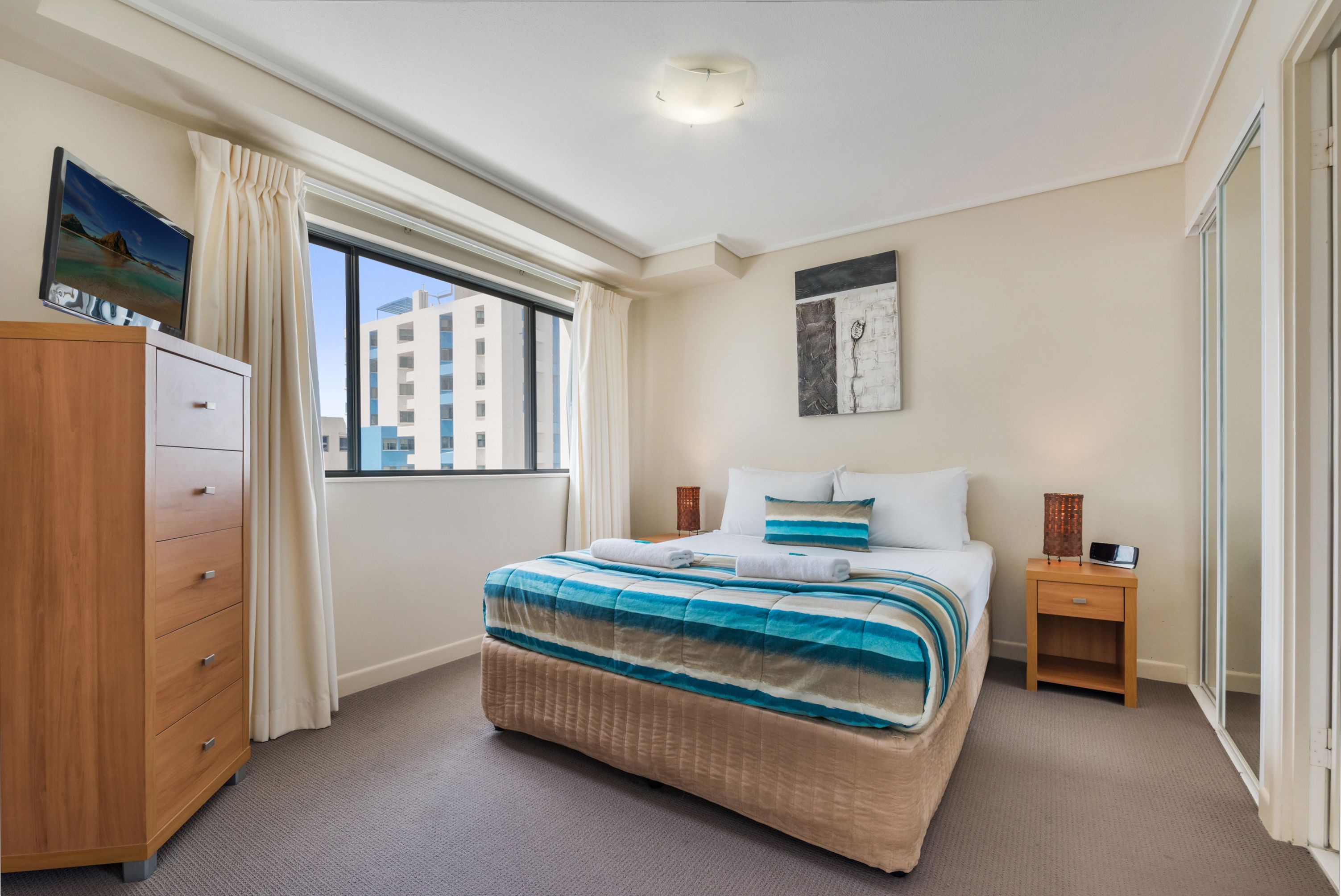 Une chambre d’hôtel avec un grand lit, une commode en bois, une table de chevet et une fenêtre avec des rideaux.