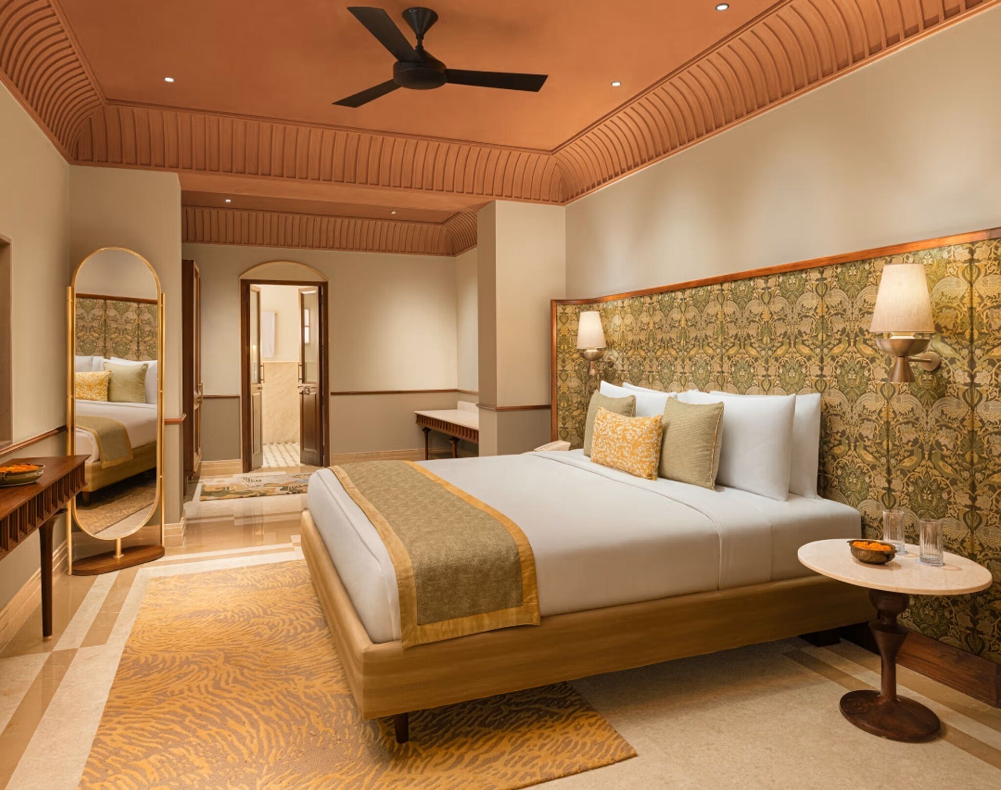 A spacious bedroom with a large bed, a ceiling fan, a mirror, a bedside table, and a round table with a lamp.