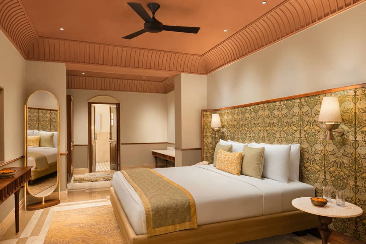 A spacious bedroom with a large bed, a ceiling fan, a mirror, a bedside table, and a round table with a lamp.