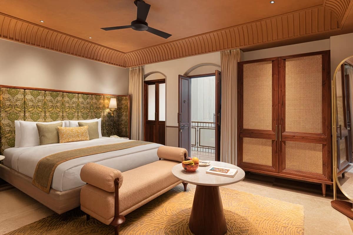 A hotel room with a bed, a sofa, a round table, a ceiling fan, and a large window with a view.