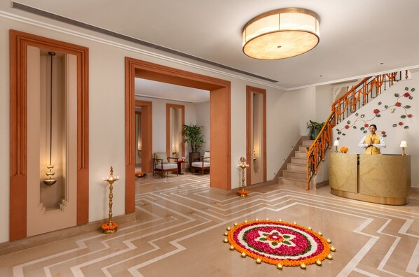 A hotel lobby with a reception desk, a staircase with decorative garlands, and a patterned floor.