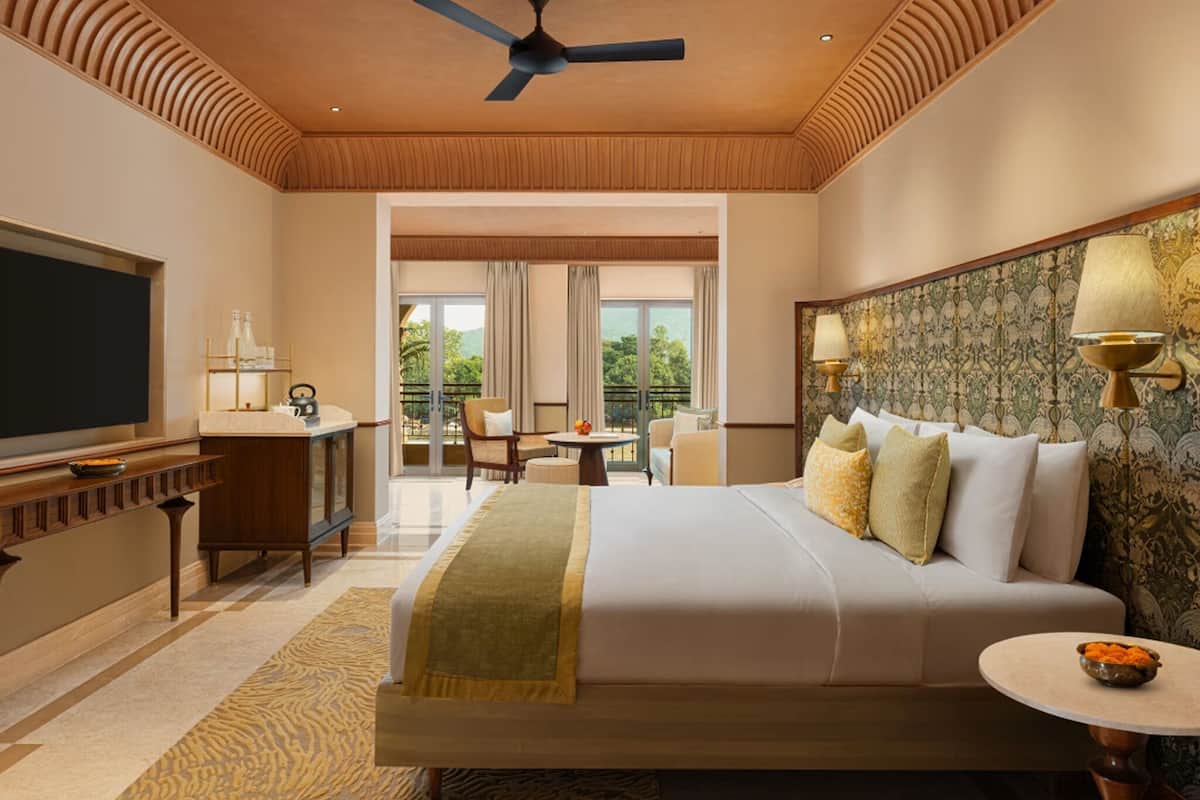 A hotel room with a large bed, a desk, a television, and a balcony with a view.