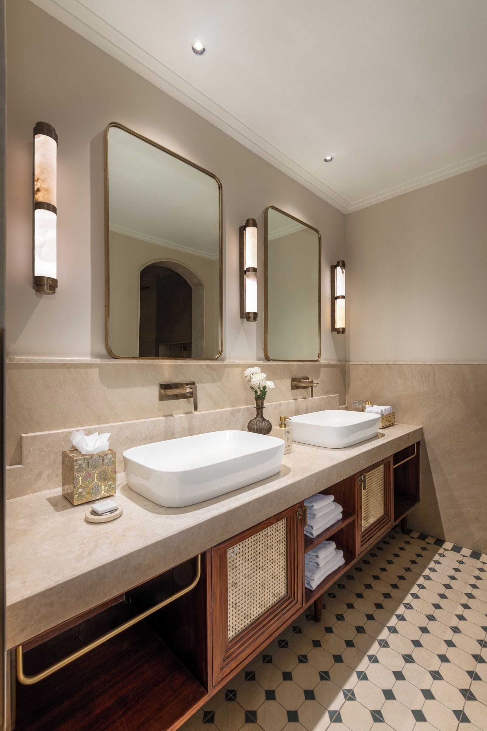 Un baño moderno con dos lavamanos, un espejo grande, apliques de pared y piso estampado.