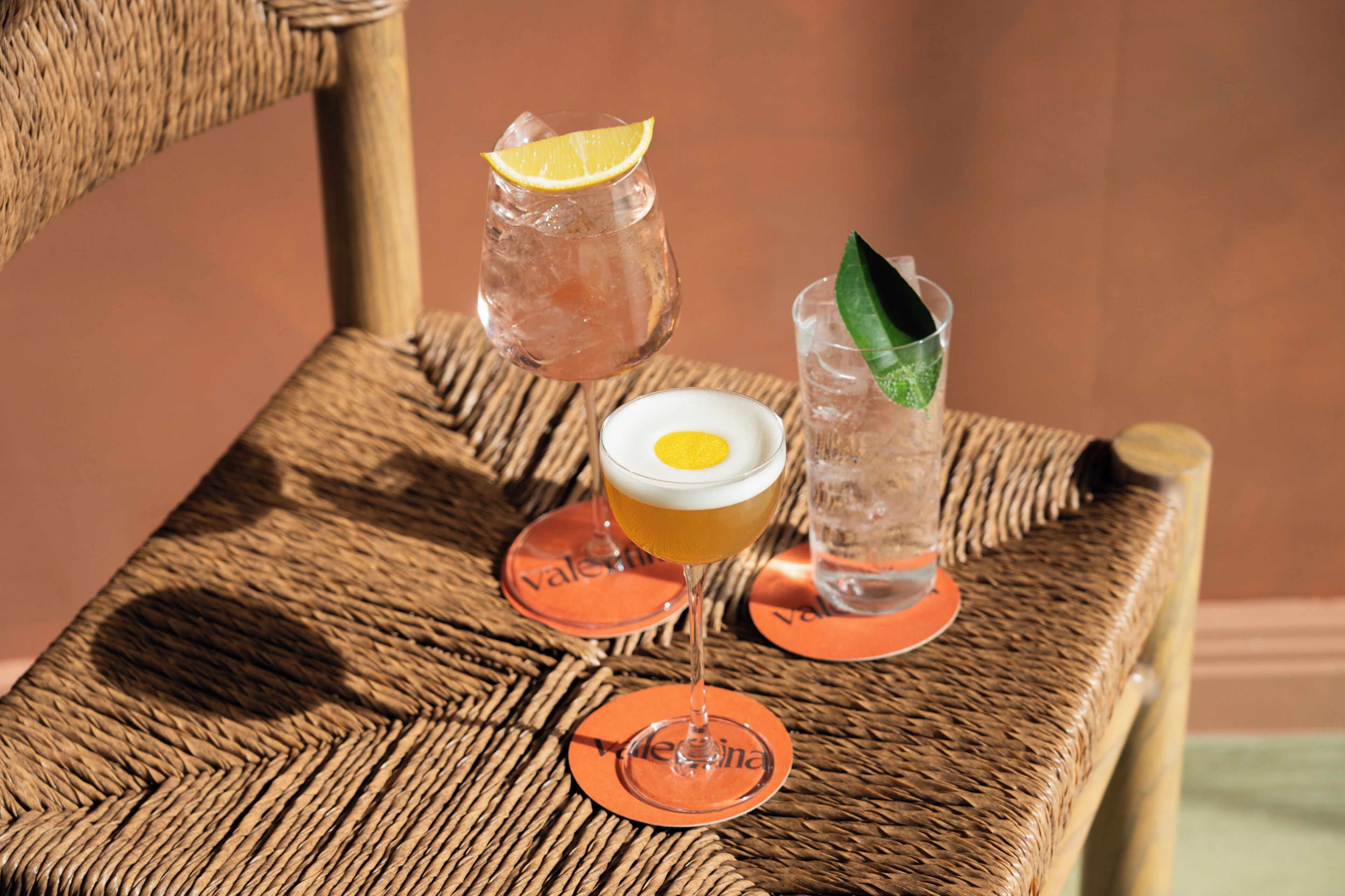 A wicker chair with three glasses of beverages, each with a coaster.
