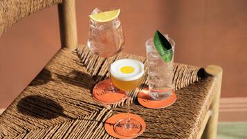 A wicker chair with three glasses of beverages, each with a coaster.