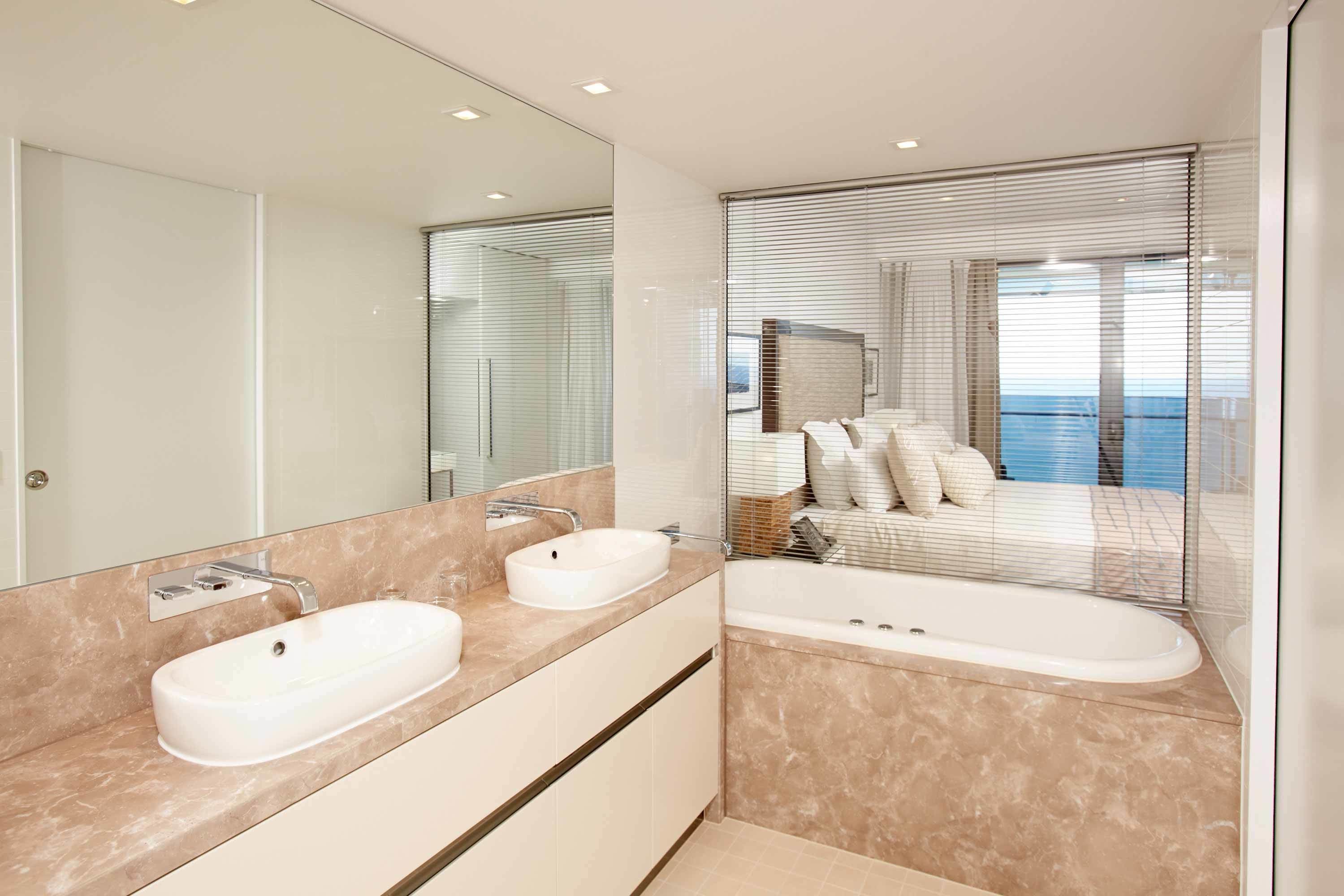 A modern bathroom with two sinks, a bathtub, and a large mirror.