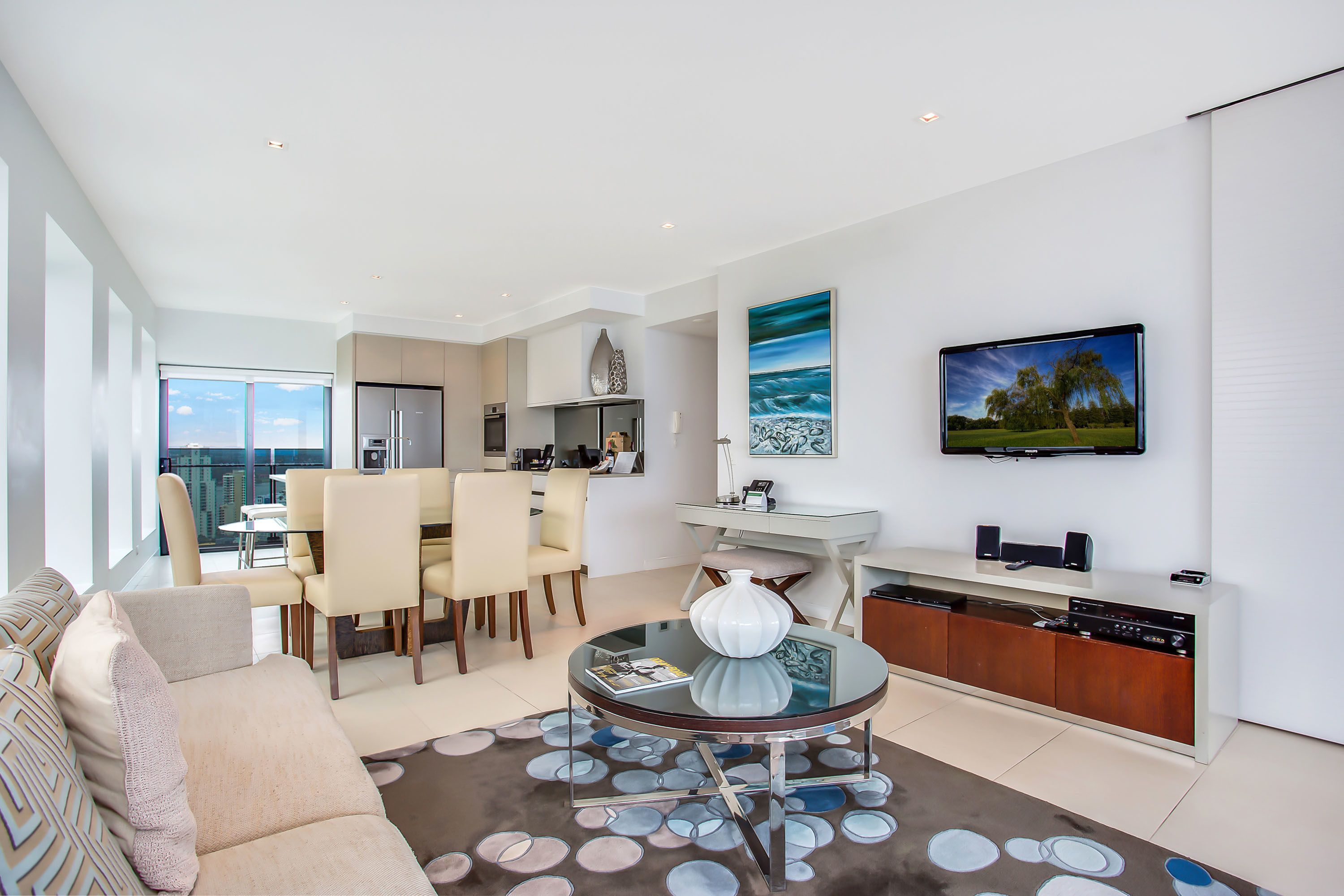 A modern living room with a dining area, a kitchen, and a large window offering a city view.