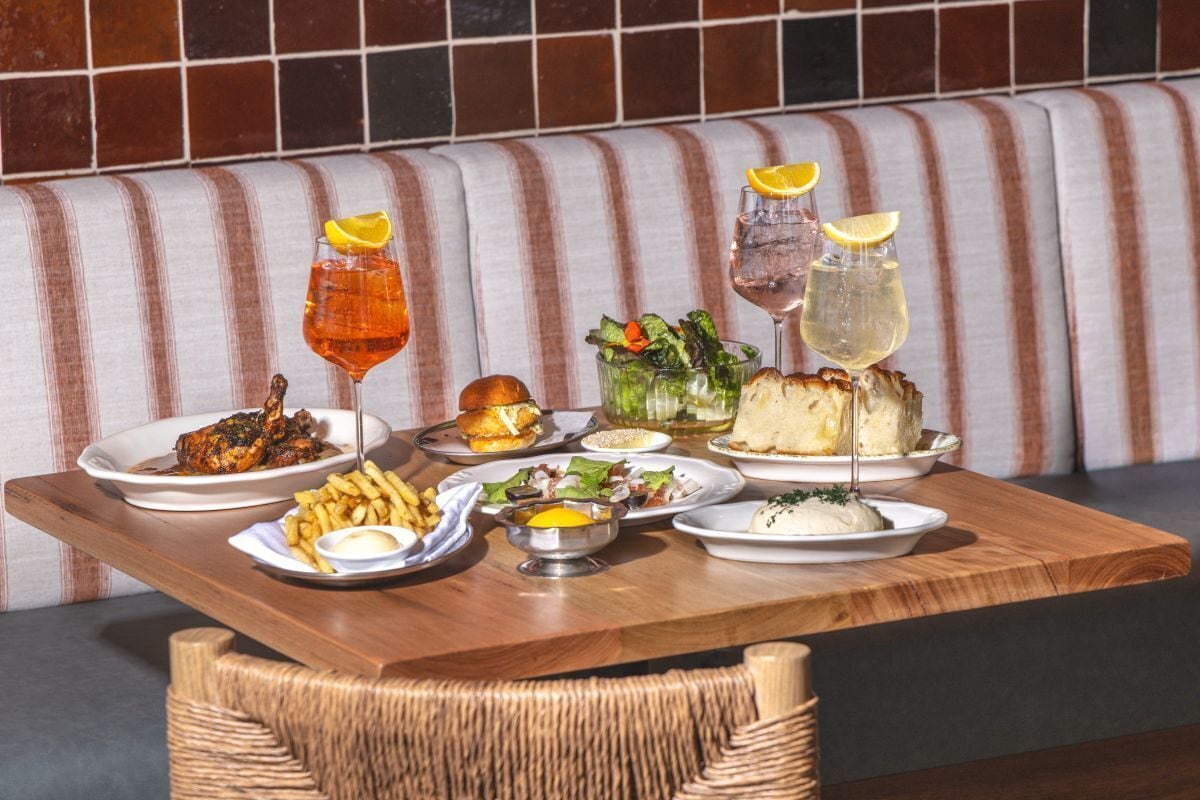 A dining table with various dishes and drinks, a wicker chair, and a striped bench in the background.