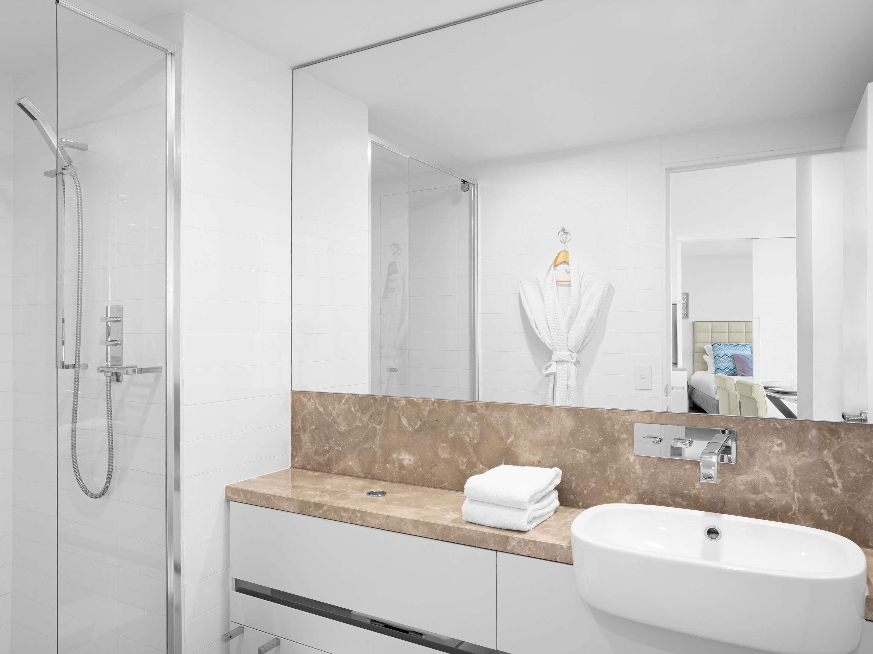Une salle de bain moderne avec une douche à parois de verre, un lavabo blanc, un comptoir en marbre et un grand miroir.