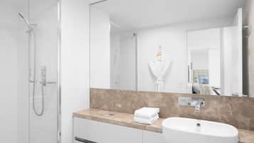 A modern bathroom with a glass-enclosed shower, a marble countertop, a sink, and a large mirror.