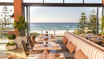 An outdoor dining area with tables and chairs, a long bench, and a view of the ocean.