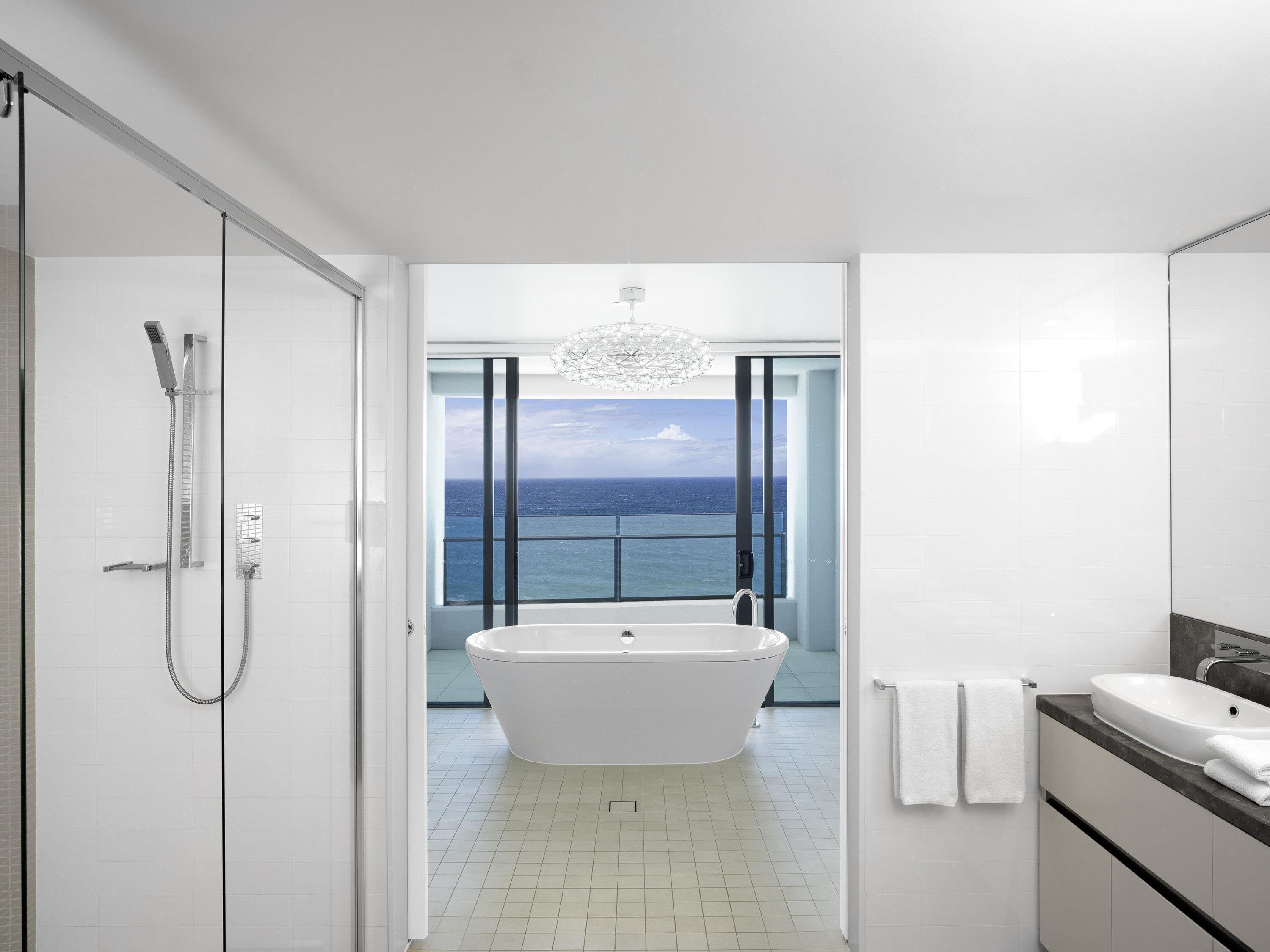 A modern bathroom with a freestanding bathtub, a shower, and a large window offering a view of the ocean.