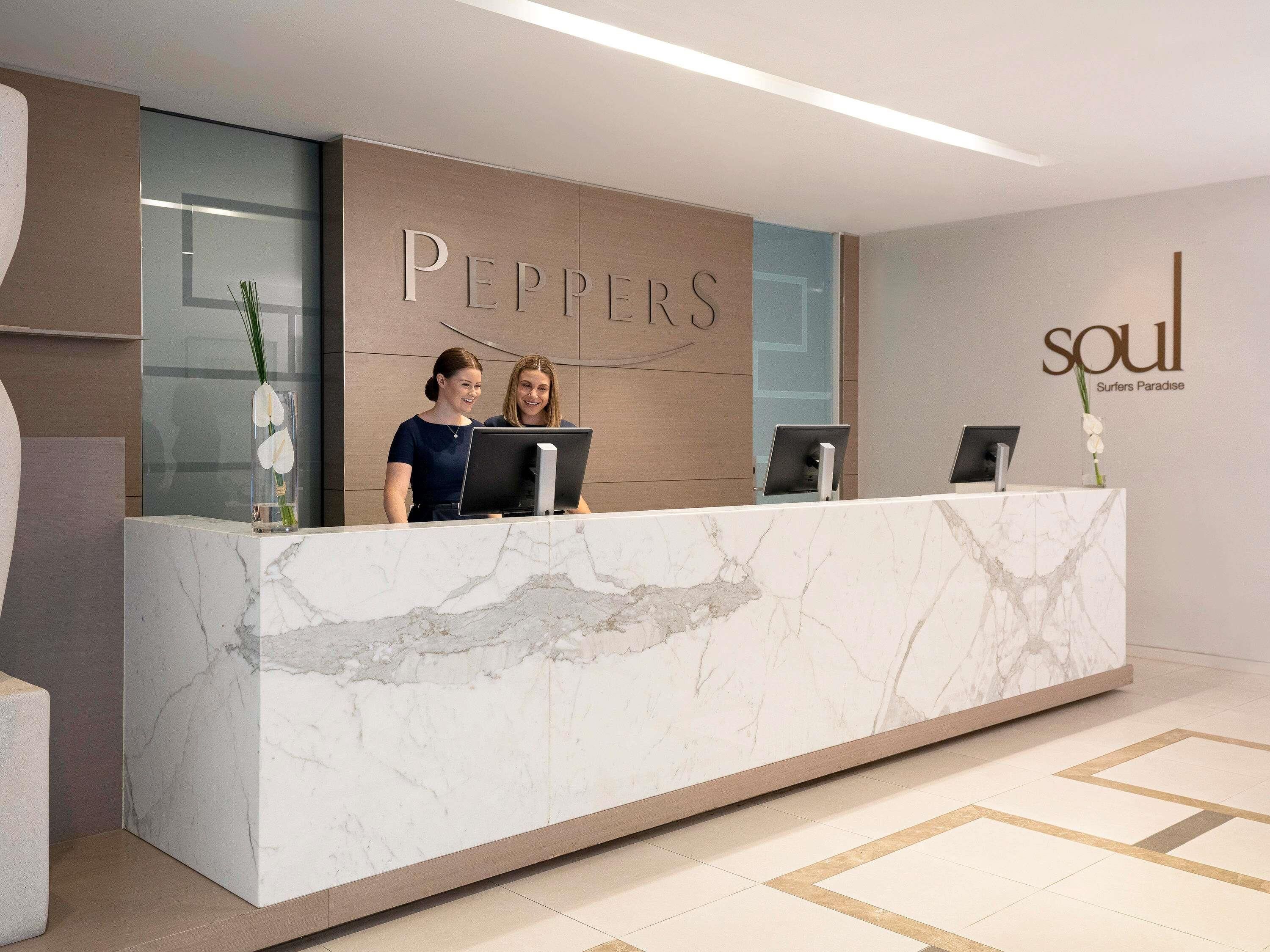 A reception desk with a marble top, two staff members, and a wall with the name 'PEPPERS' and 'soul Surfers Paradise' signage.