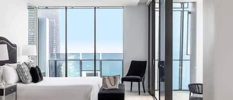 A modern hotel room with a large bed, a desk, a chair, and a view of the city.