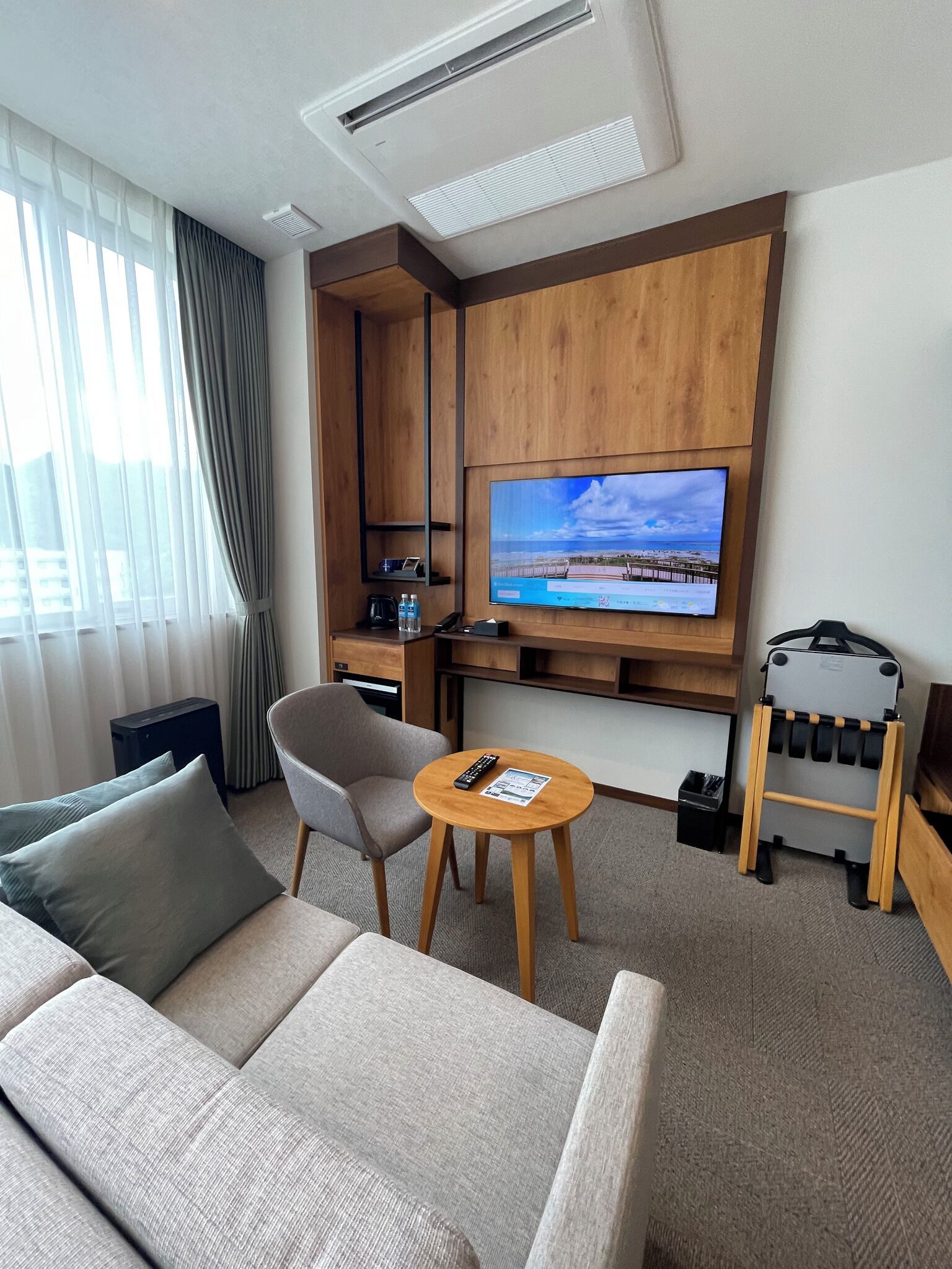 A hotel room with a sofa, a small round table, a TV mounted on the wall, and a mini-fridge.