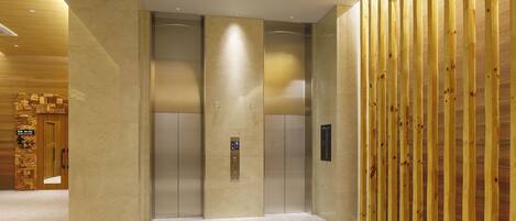 A modern elevator area with a wooden panel wall and a marble floor.