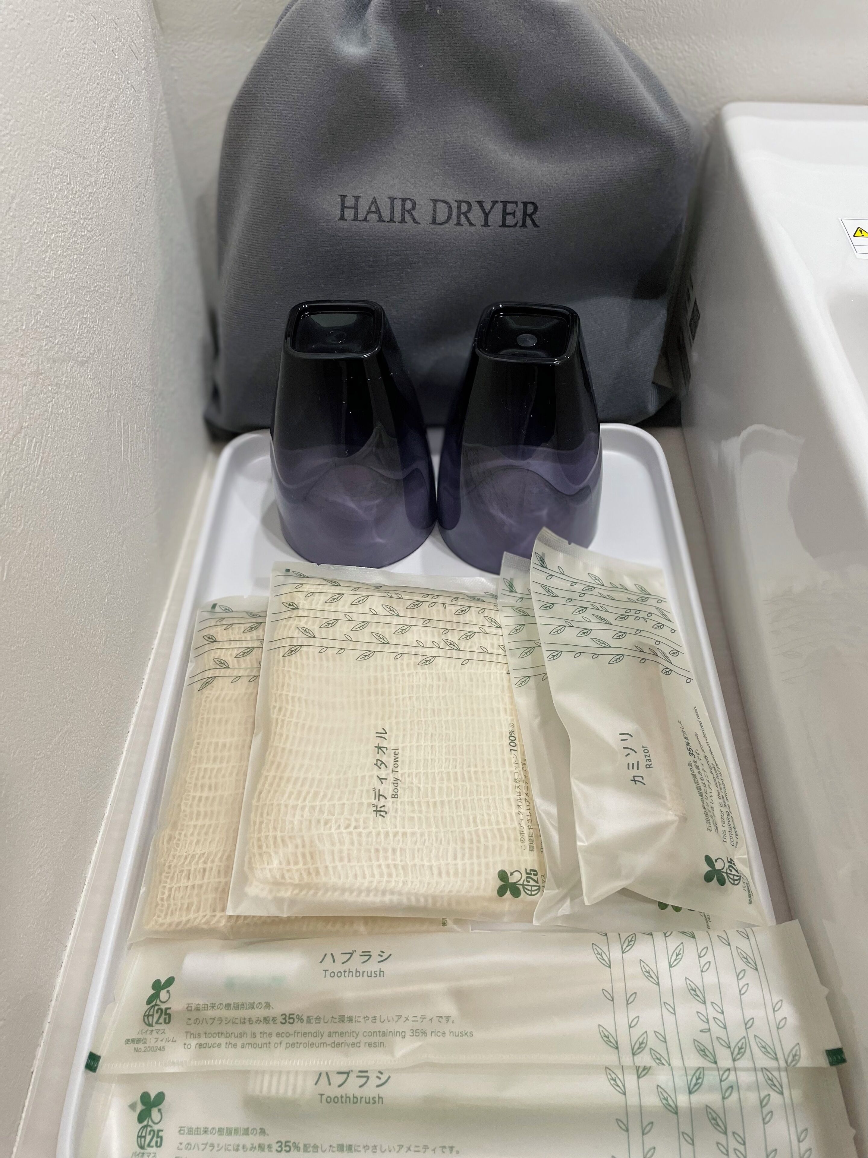 Un baño con un secador de pelo, dos botellas y una toalla con texto en japonés.