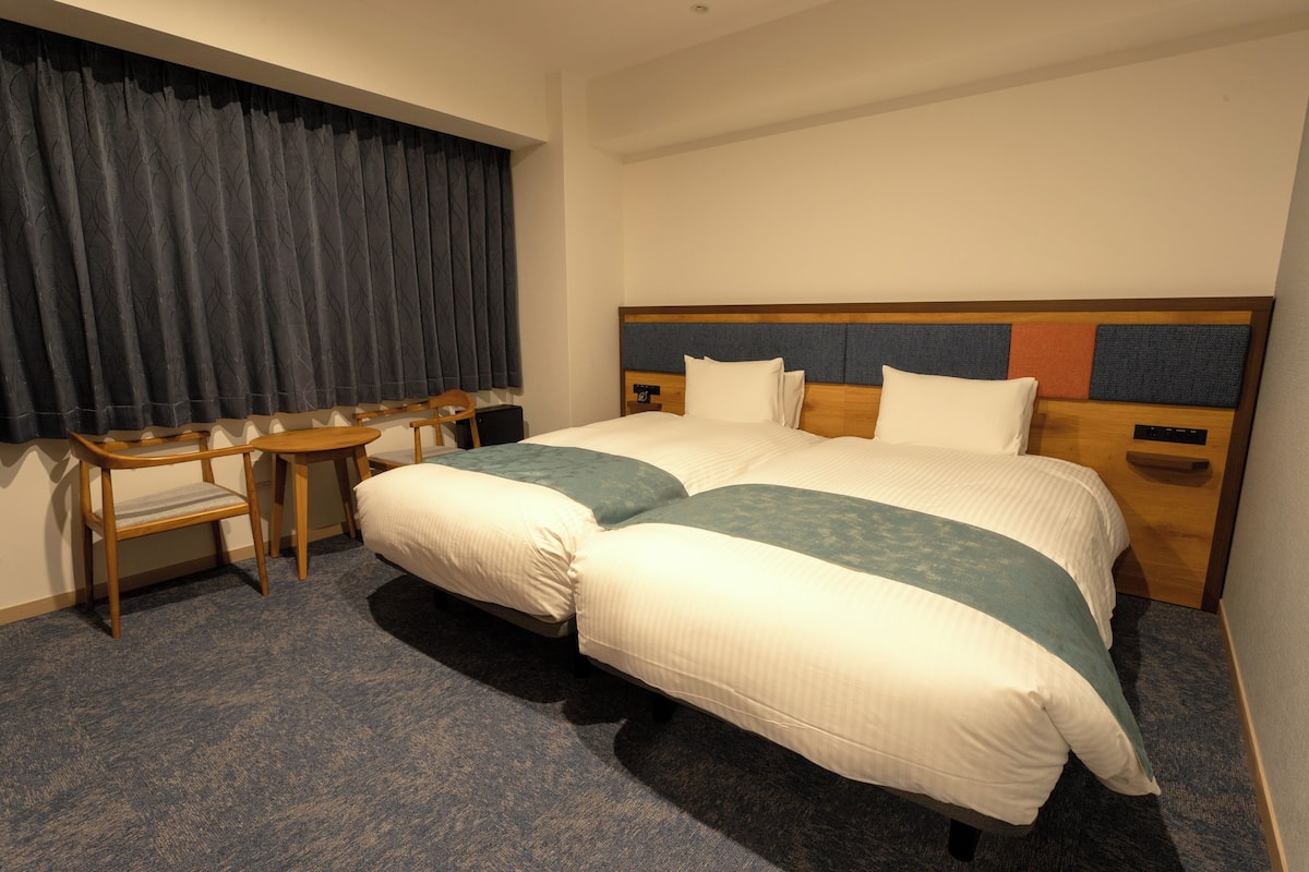 Habitación de hotel con dos camas, un escritorio y una silla.