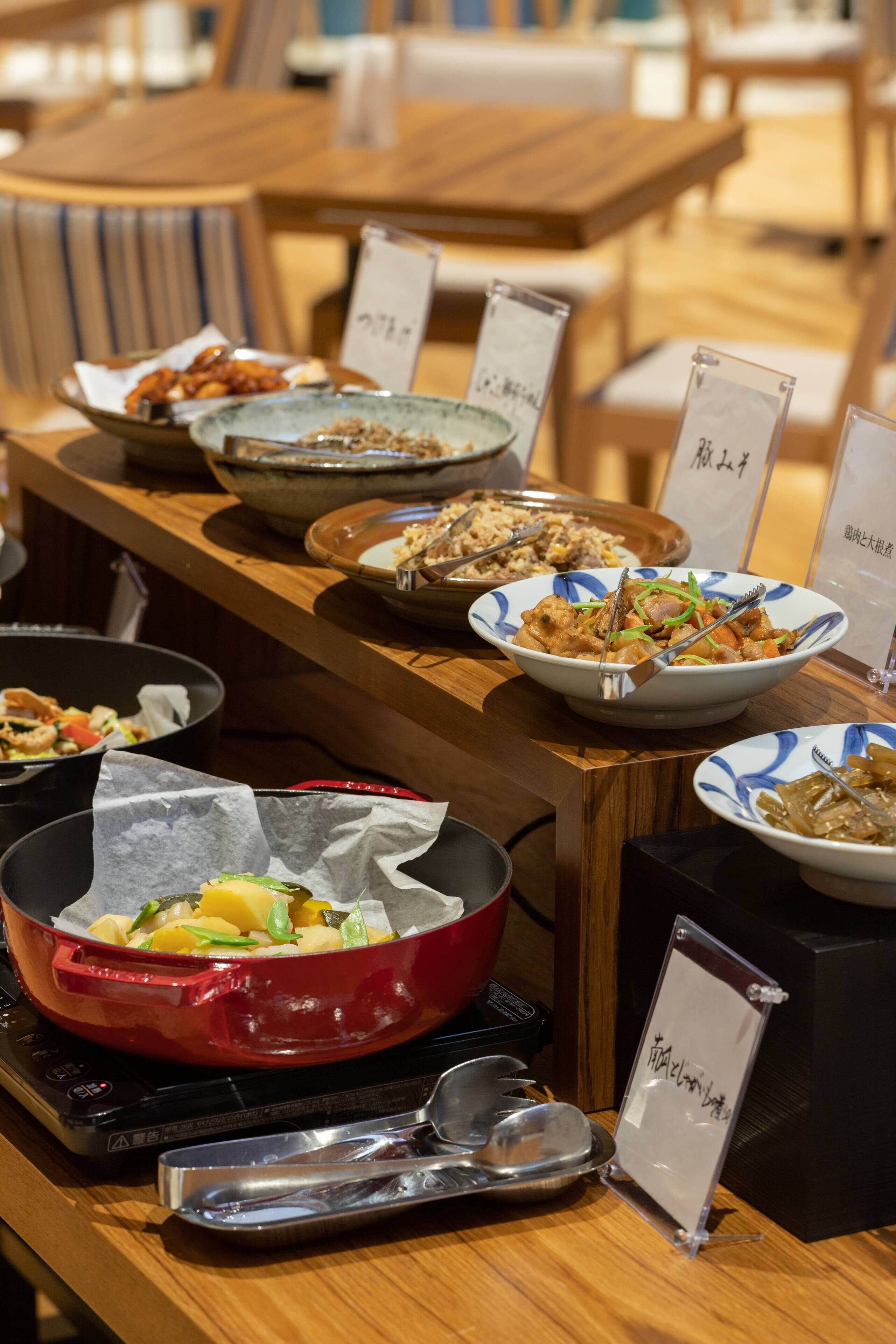 Una mesa de buffet con diversos platos y una olla roja sobre una estufa portátil.