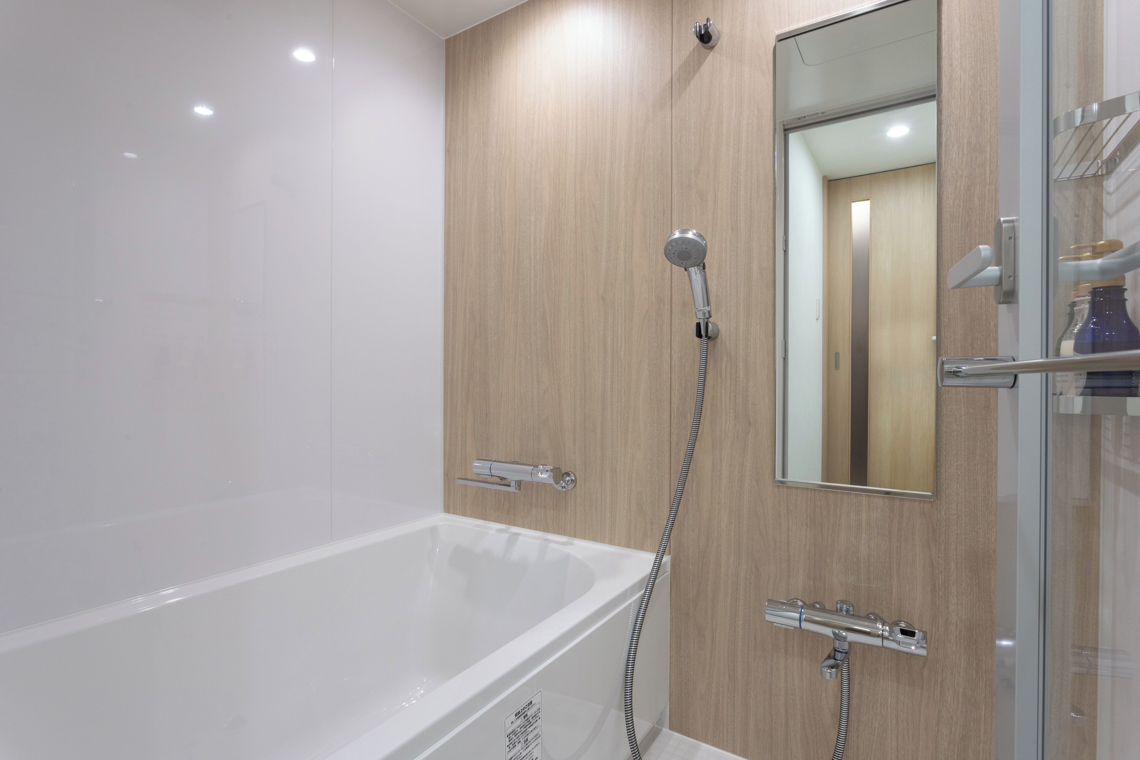 A modern bathroom with a white bathtub, a glass shower enclosure, and a wooden wall panel.