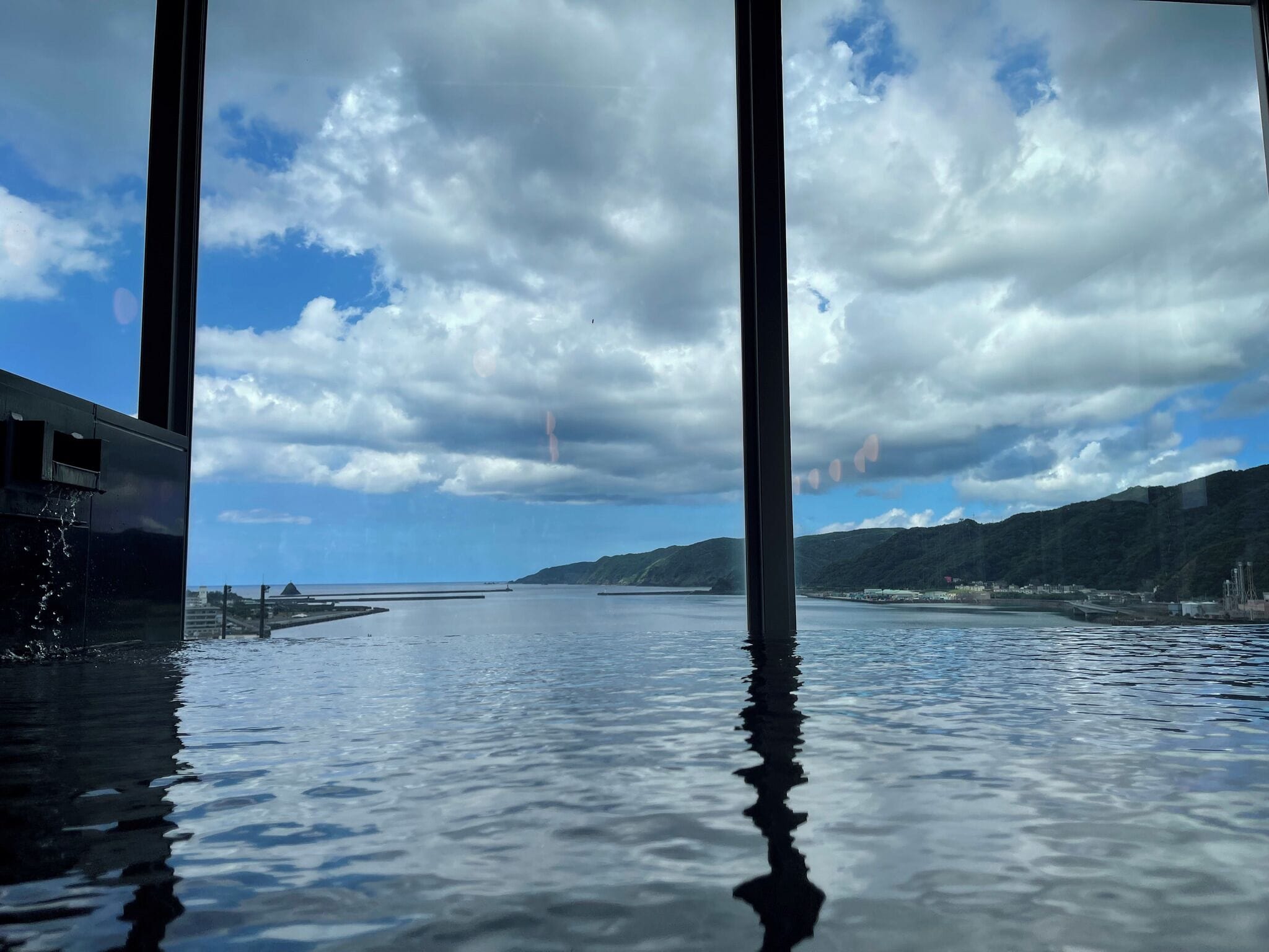 Une vue depuis une fenêtre donnant sur une étendue d’eau calme, avec une côte et des montagnes visibles au loin.
