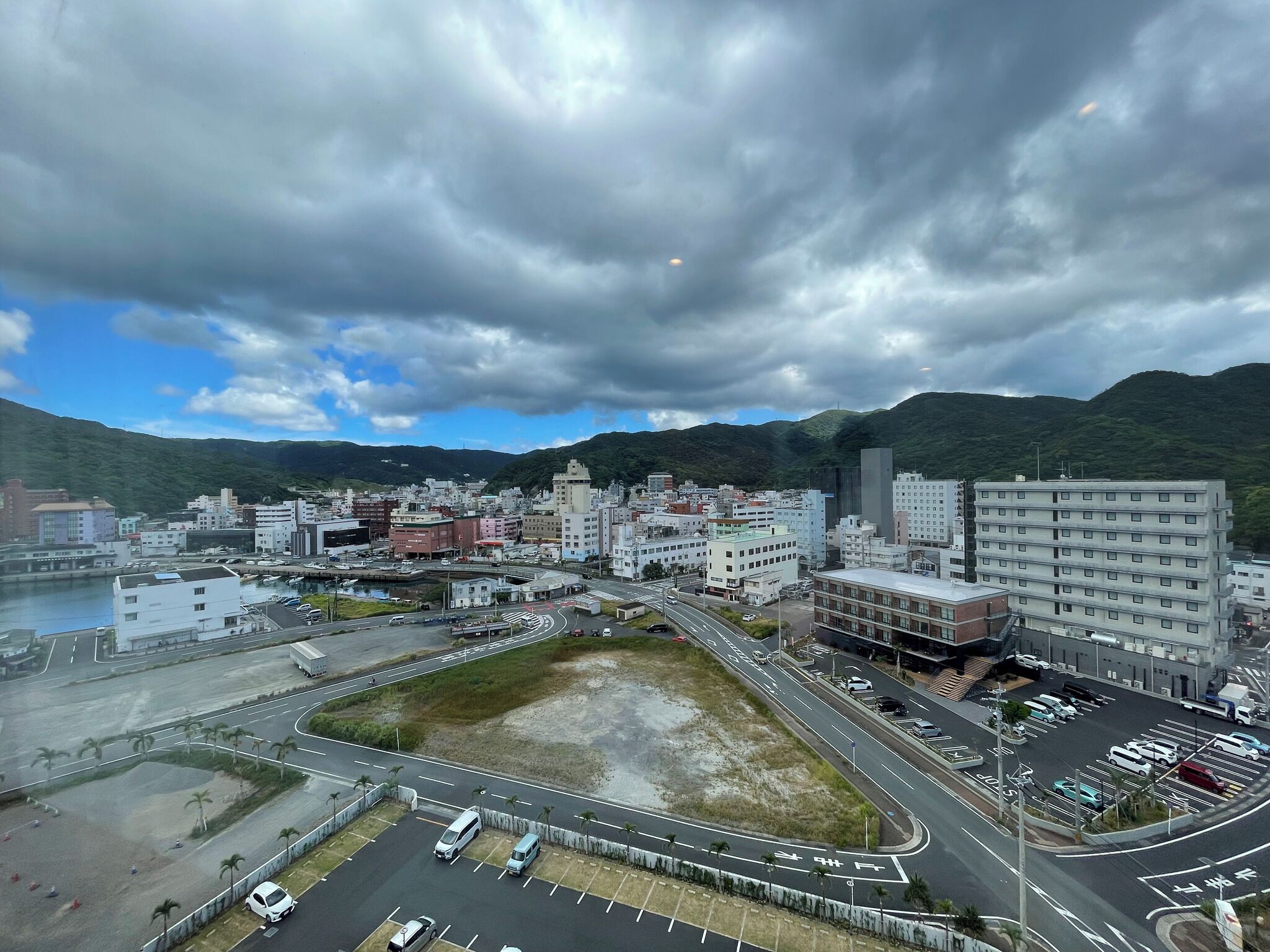 A cityscape with a mix of modern and traditional buildings, a parking lot, and a road leading to a bridge.