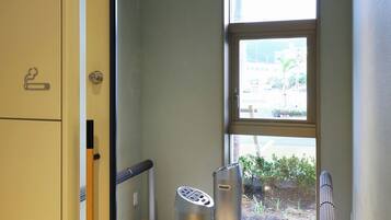 A hallway with a large window, a door with a smoke detector, and two cylindrical objects on the floor.
