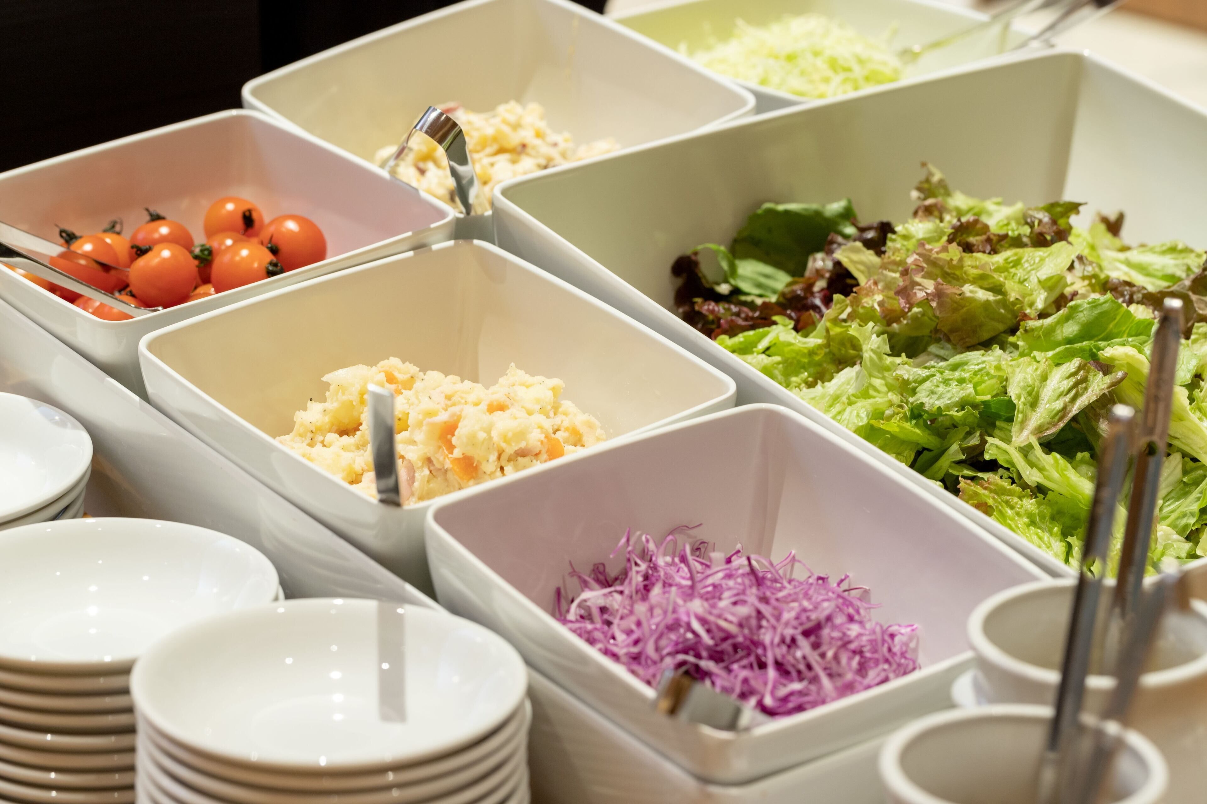 A buffet with various food items in separate containers, including tomatoes, coleslaw, and a salad.
