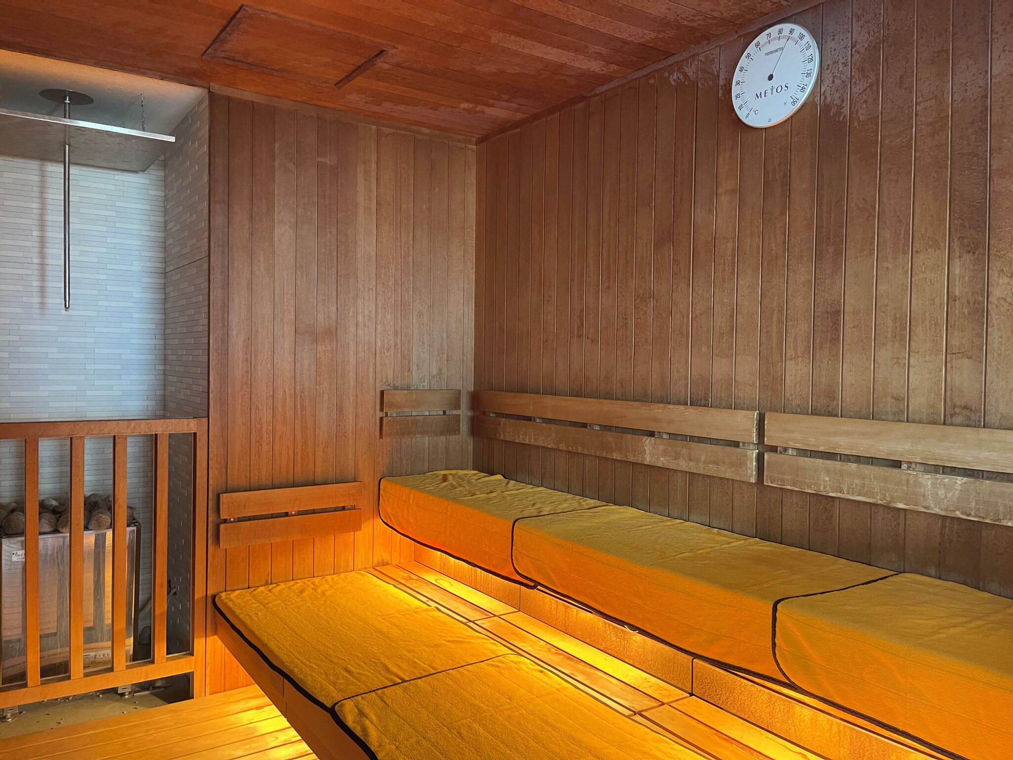 A sauna room with wooden benches and a wall-mounted thermometer.
