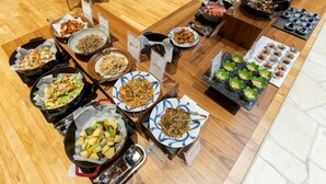 Un bufé con diversos platos, incluyendo frituras, ensaladas y postres, dispuesto sobre una mesa de madera.