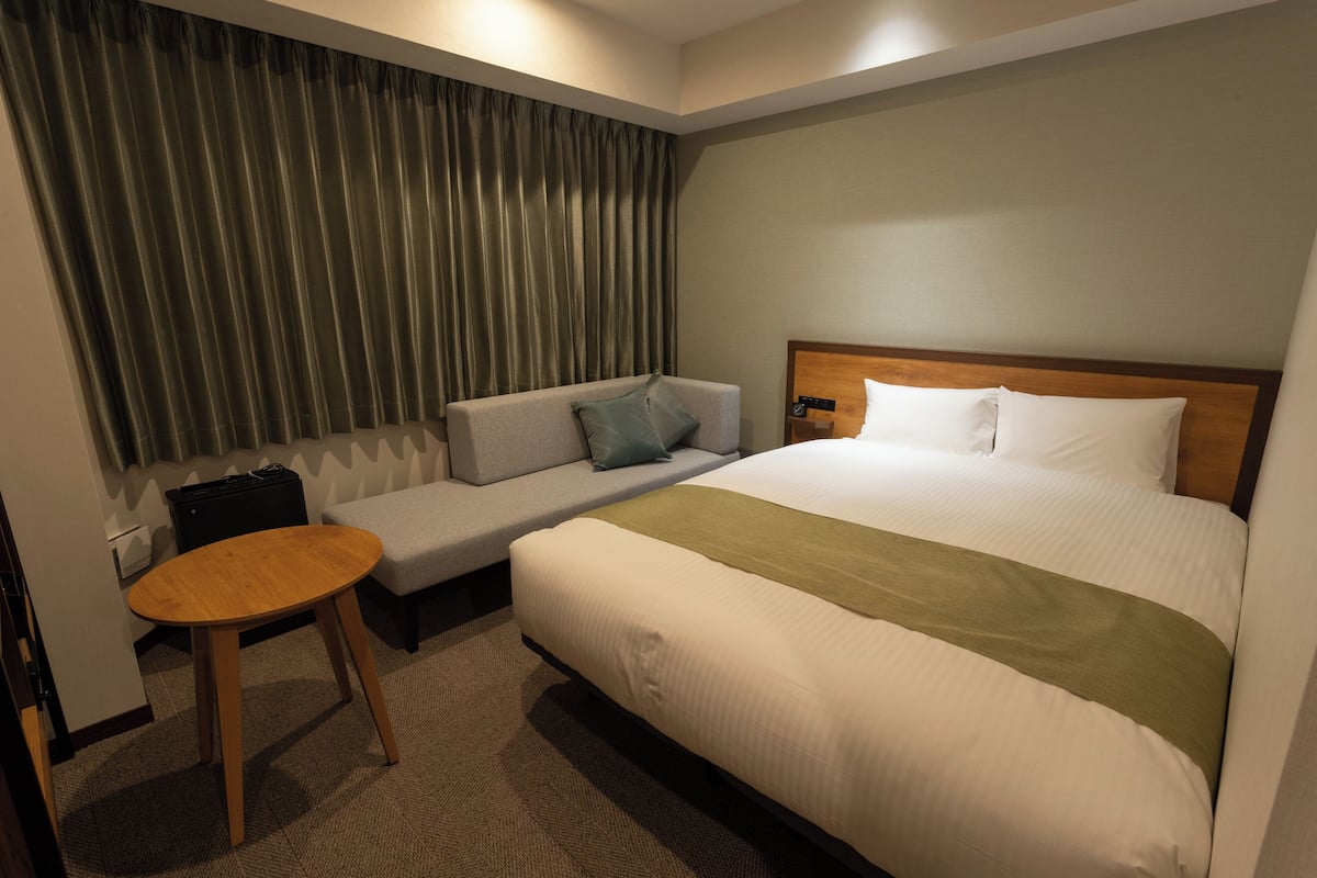 Una habitación de hotel con cama, sofá, una mesita y una cortina.