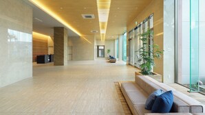 Un vestíbulo amplio con techo de madera, una zona de estar con cojines y una planta grande.