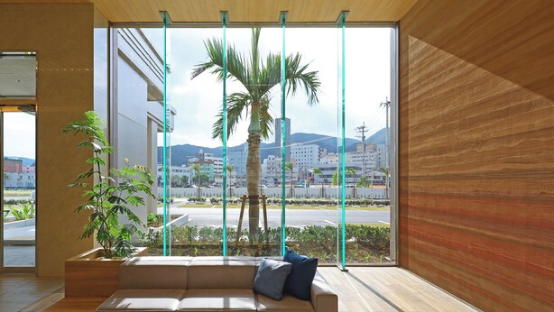 Un interior moderno con un sofá, una planta en maceta y vistas de un paisaje urbano a través de amplios ventanales.