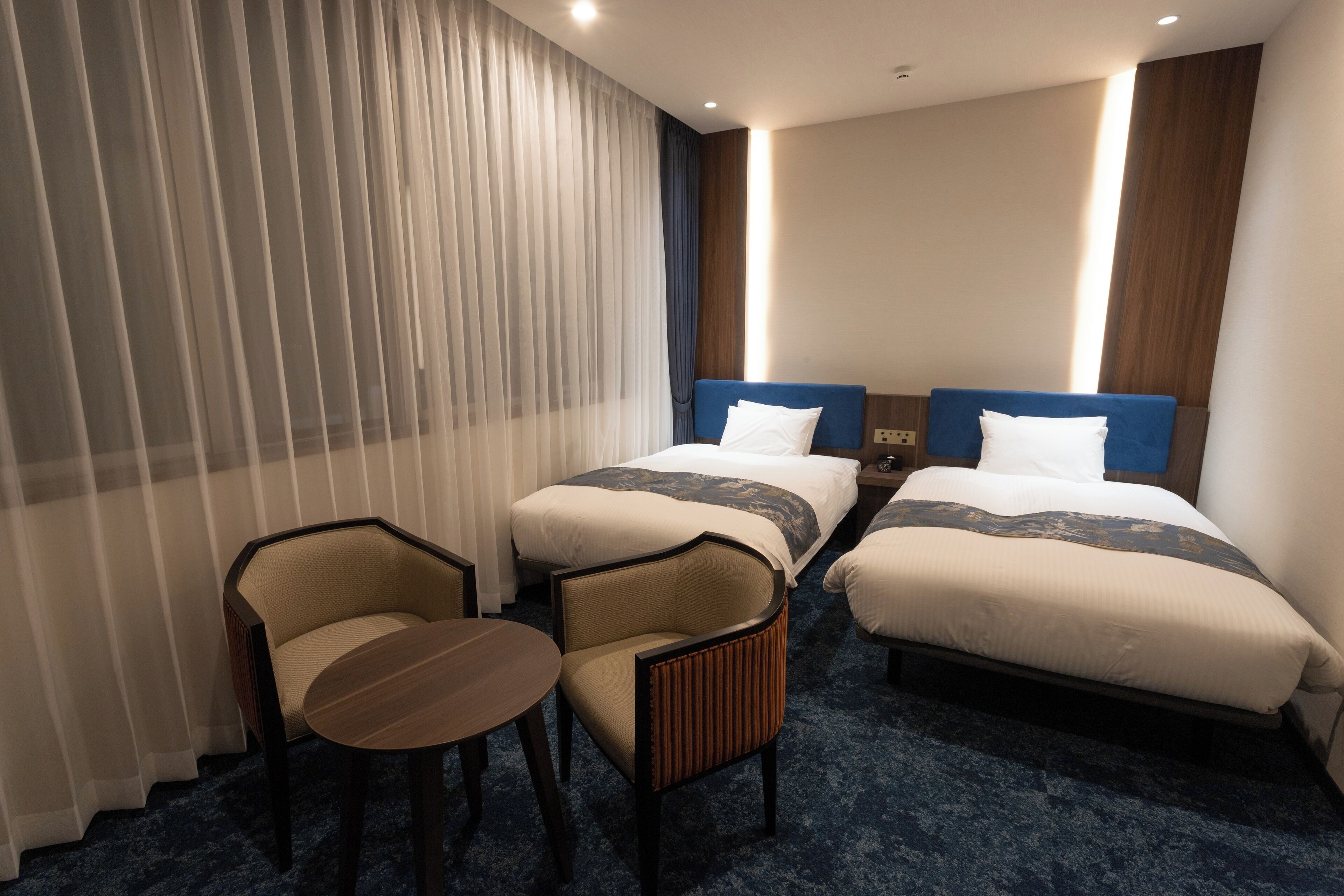Habitación de hotel con dos camas, una mesita y una silla.