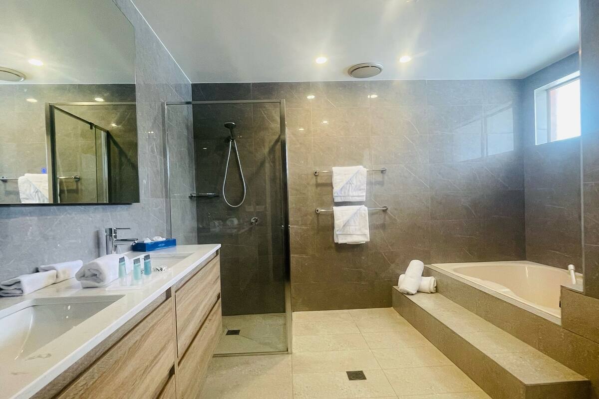 A modern bathroom with a glass-enclosed shower, a large mirror, and a bathtub.