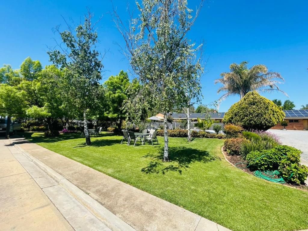 Ein Wohngebiet mit gepflegtem Rasen, einer Terrasse mit Gartenmöbeln und verschiedenen Bäumen und Sträuchern.