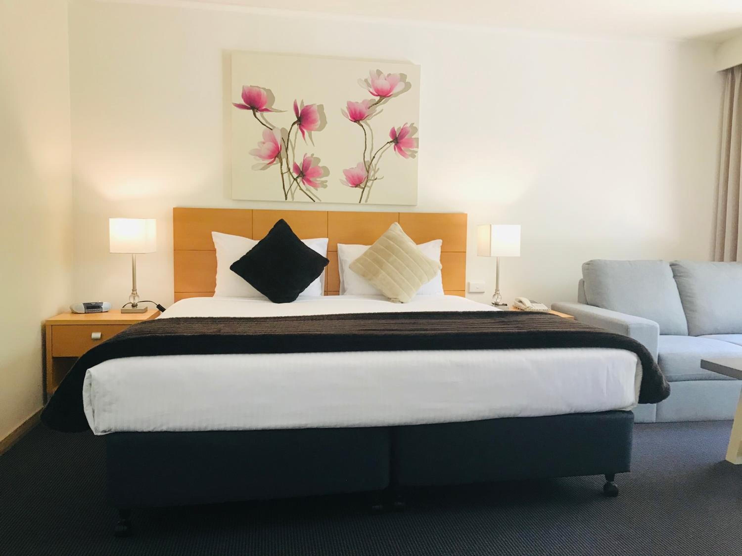 Habitación de hotel con una cama grande, dos mesitas de noche, una silla y un cuadro colgado en la pared.