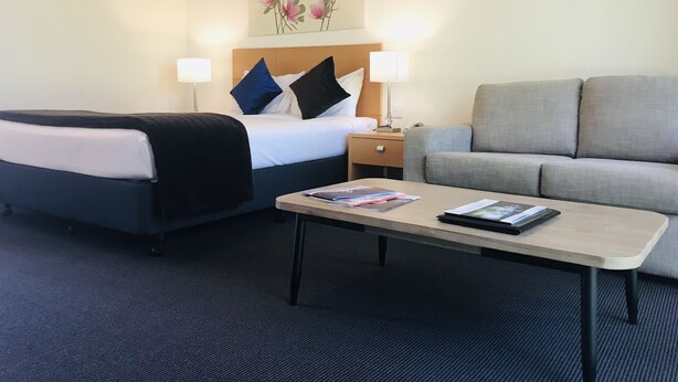 A hotel room with a bed, two bedside lamps, a sofa, and a coffee table. - Nagambie Motor Inn (Nagambie)