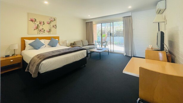 A hotel room with a bed, a desk, a chair, a TV, and a window with curtains. - Nagambie Motor Inn (Nagambie)