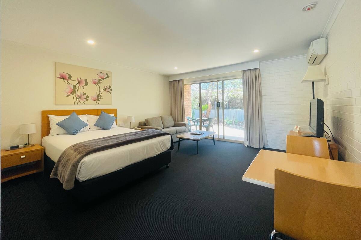 A hotel room with a bed, a desk, a chair, a TV, and a window with curtains.
