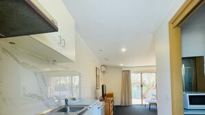 A modern kitchen with white cabinets, a black stove, and a built-in oven. There is a dining area with a table and chairs visible through an open door. - Nagambie Motor Inn (Nagambie)