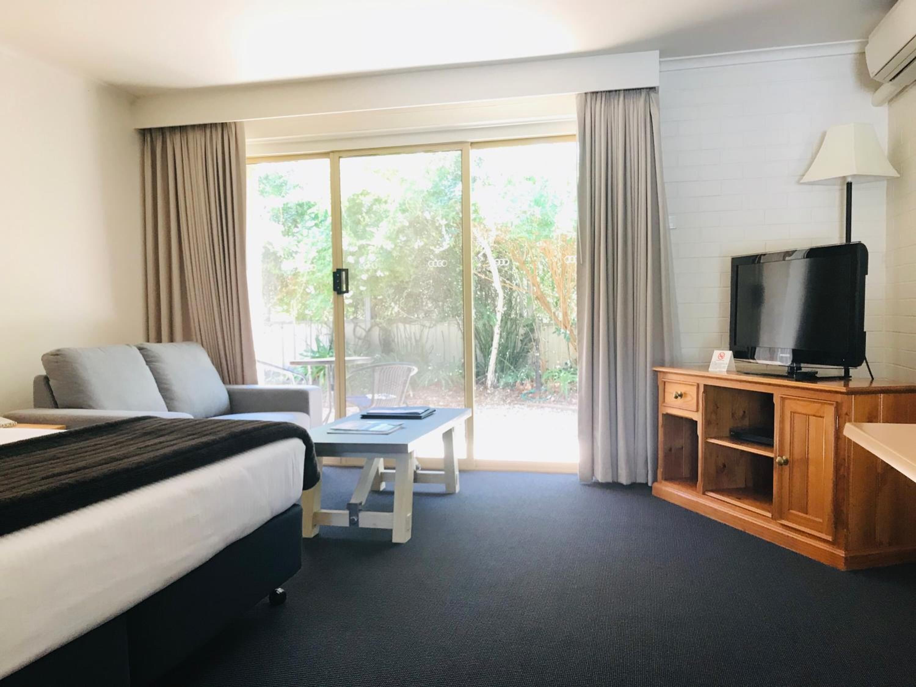 A hotel room with a bed, a sofa, a TV, a desk, and a sliding glass door to a balcony.