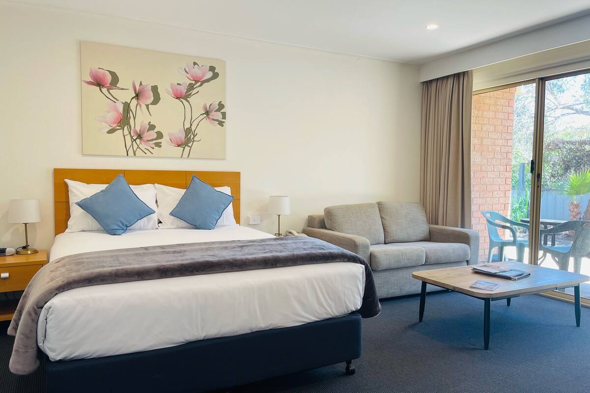 A hotel room with a bed, a sofa, a coffee table, and a painting of flowers on the wall.