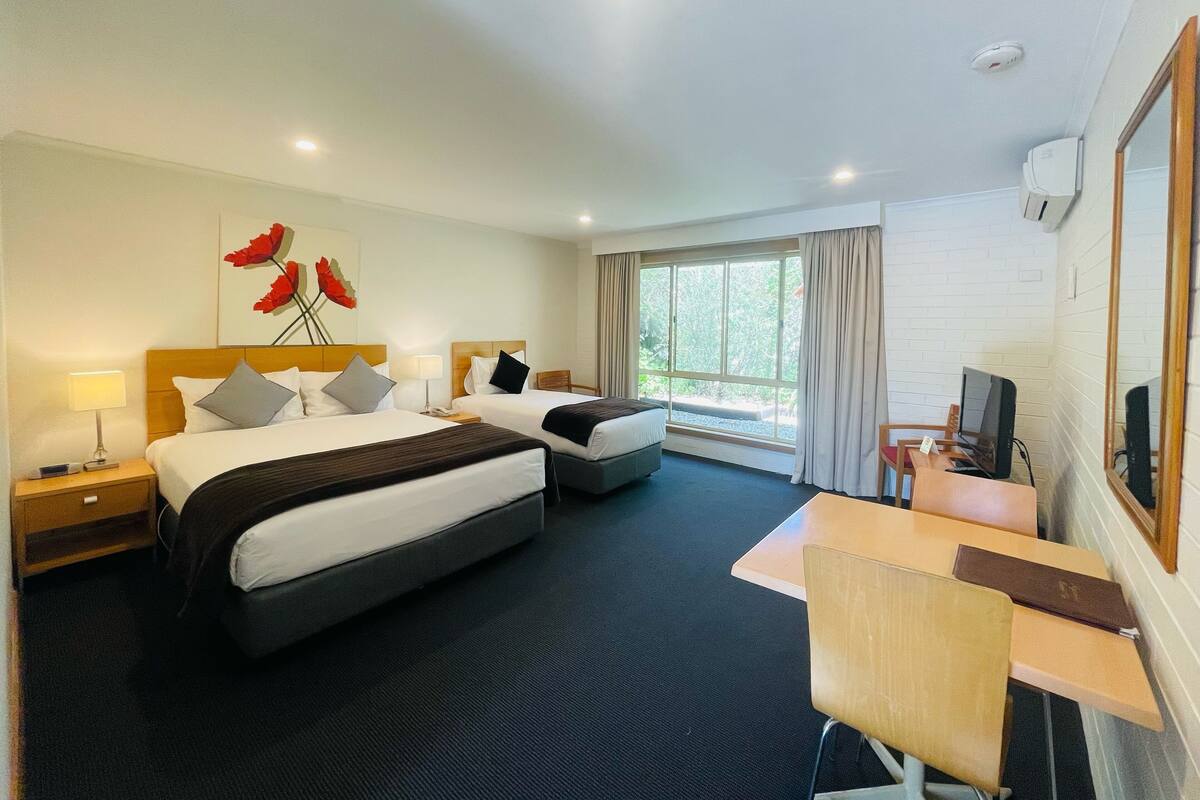 A hotel room with two beds, a desk, a chair, a TV, and a window with curtains.