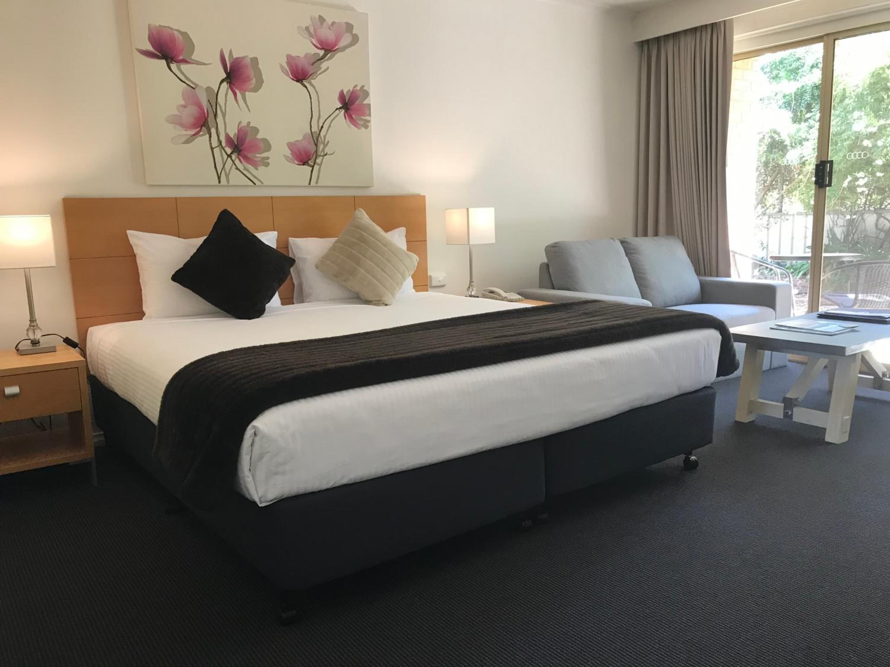 A hotel room with a large bed, a desk, a chair, and a window with curtains.