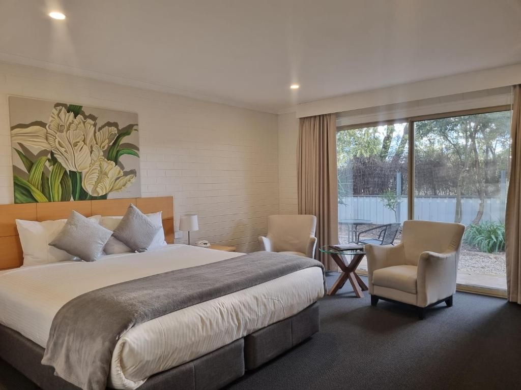 A hotel room with a large bed, two armchairs, a small table, and a window with a view of trees.
