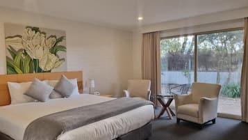 A hotel room with a large bed, two armchairs, a small table, and a window with a view of trees.
