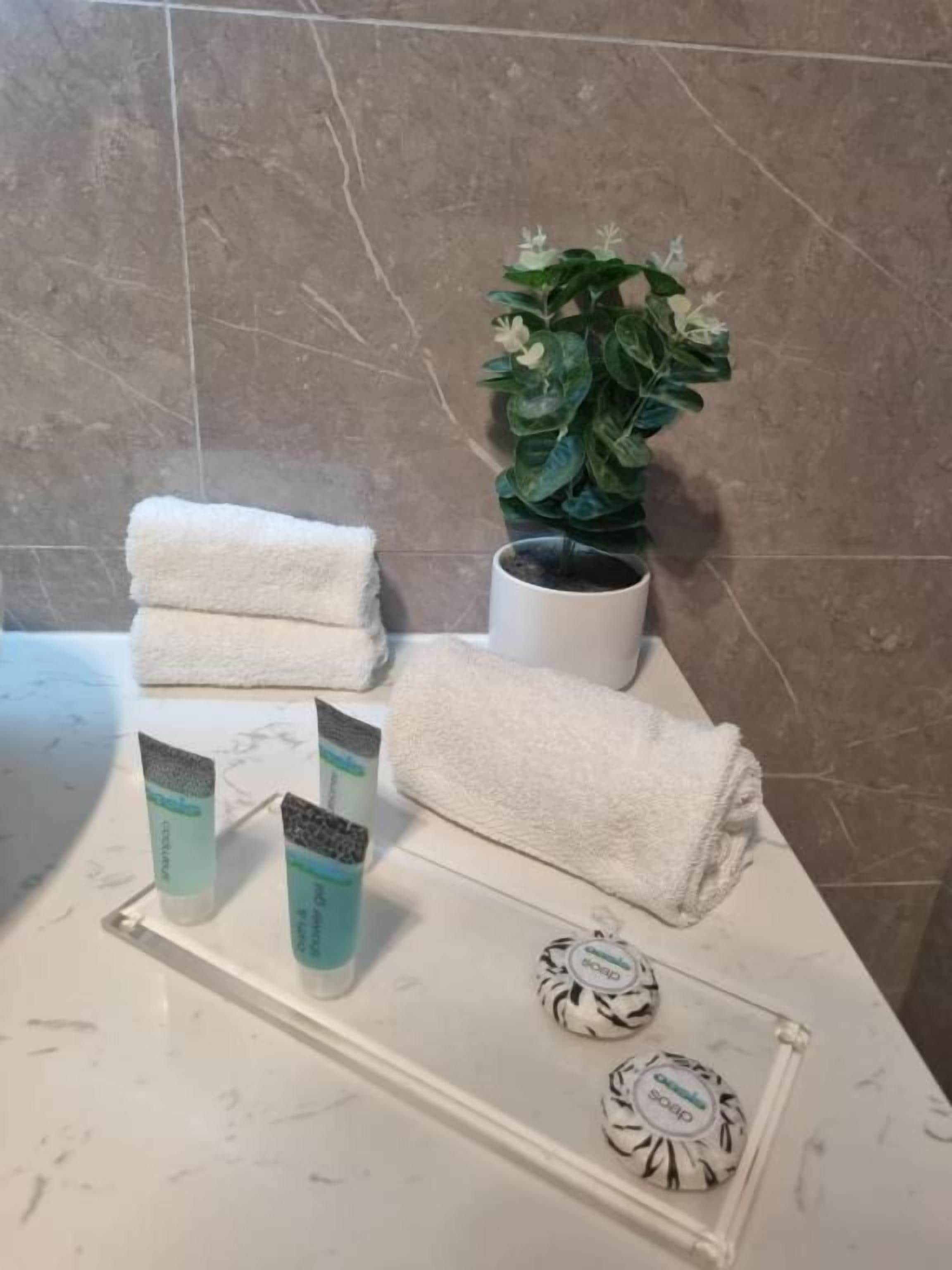Uma bancada de banheiro com tampos de mármore, uma toalha branca, uma planta em vaso e artigos de higiene pessoal.