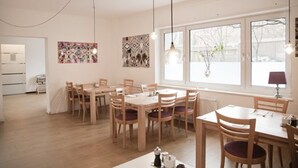 A dining area with wooden tables and chairs, large windows with a view of the outside, and artwork on the walls. - Hotel Les Nations (Berlin)